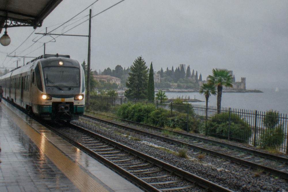A regional train pulling into Peschiera del Garda station with the lake beyond the platform