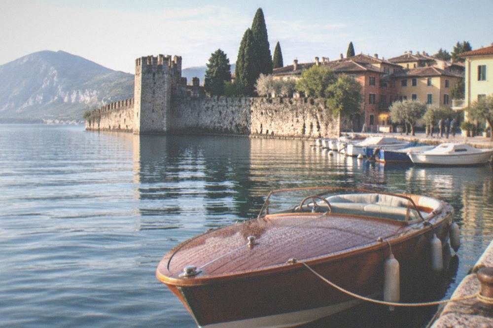 A wooden boat moored at a stone pier on Lake Garda with a walled town behind it