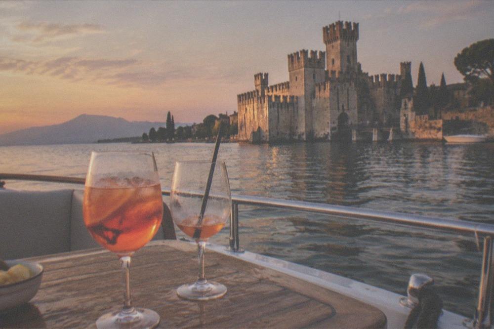An aperitivo glass on a boat deck with the Sirmione castle and evening light across the water