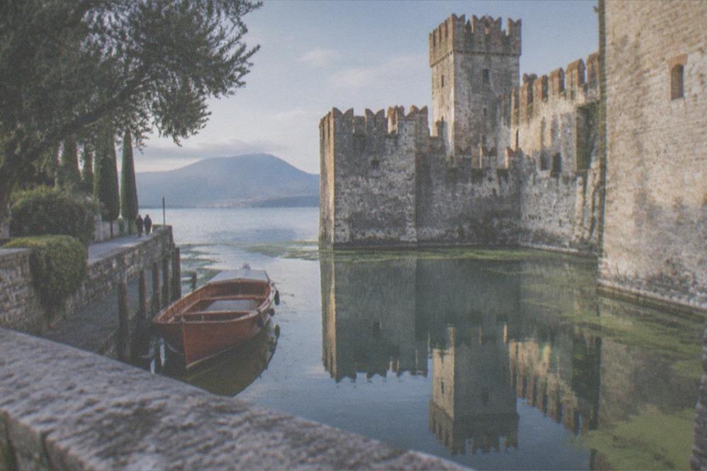 A wooden boat on Lake Garda near a castle waterfront in soft autumn light