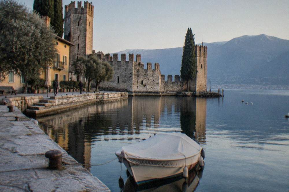 A small covered boat moored at a stone pier on Lake Garda on a still winter morning