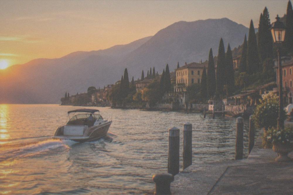 A skippered charter boat at golden hour on Lake Garda with a village and mountains in the distance