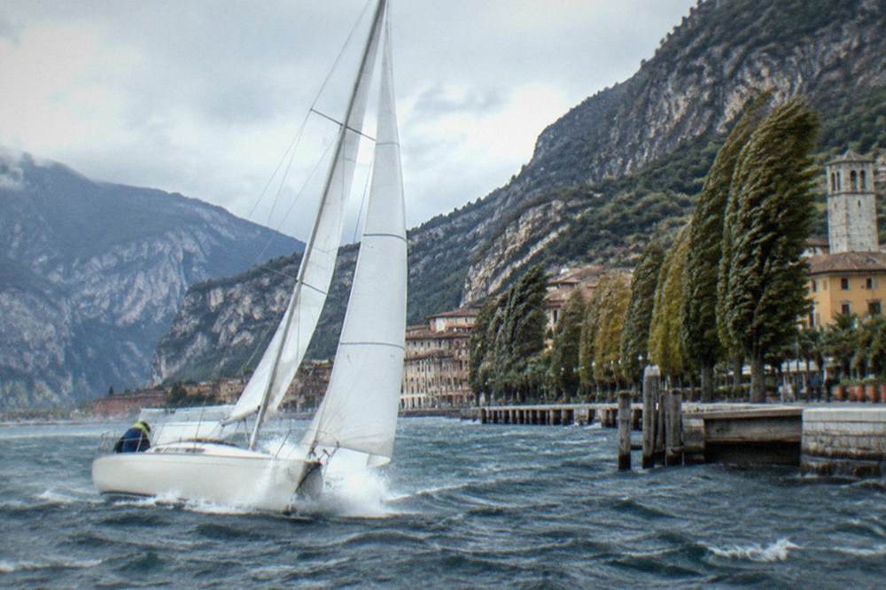 A sailboat running before a fresh breeze on Lake Garda with whitecaps on the water