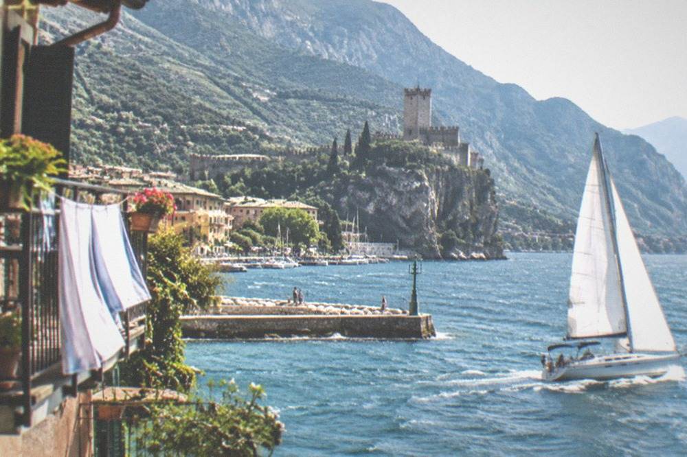 An afternoon breeze filling the sails of a boat on Lake Garda with the shore in the background