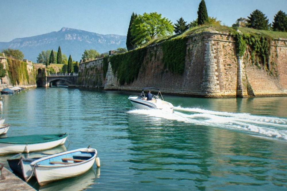 A fast open speedboat cutting through calm water near Peschiera fortress