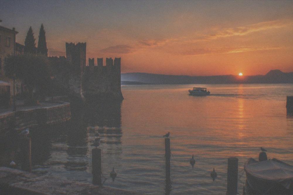 A boat underway on still water under a deep orange sky at the end of the day