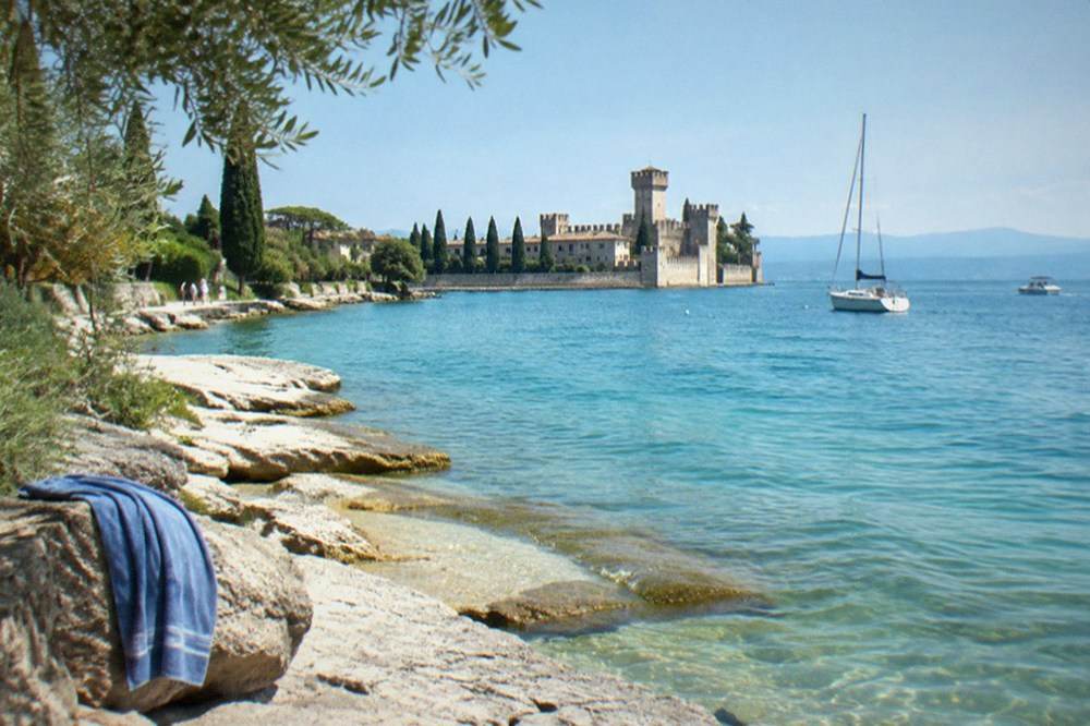 Clear turquoise water along a rocky Lake Garda shoreline on a calm summer morning