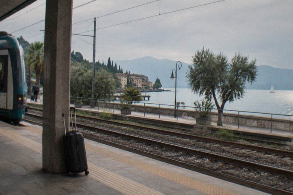 A regional train stopped at Desenzano del Garda station with the lake visible beyond the platforms
