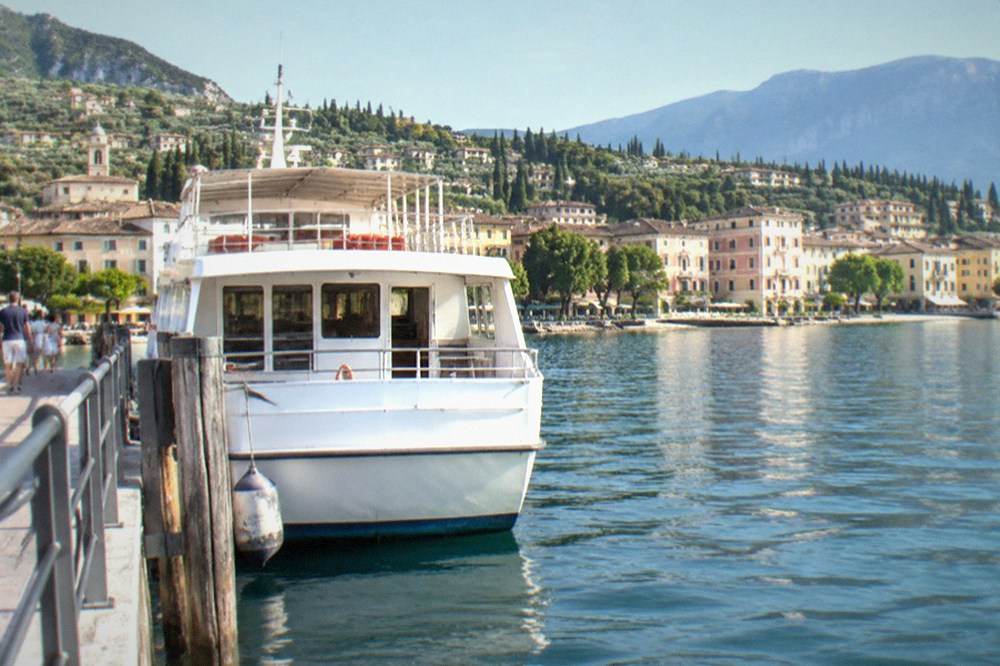 A white passenger ferry moored at a Lake Garda landing stage with a hillside town behind it