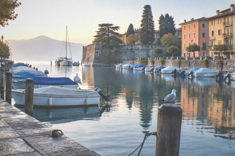 A lakeside promenade in Peschiera del Garda with moored boats and pastel buildings along the harbour