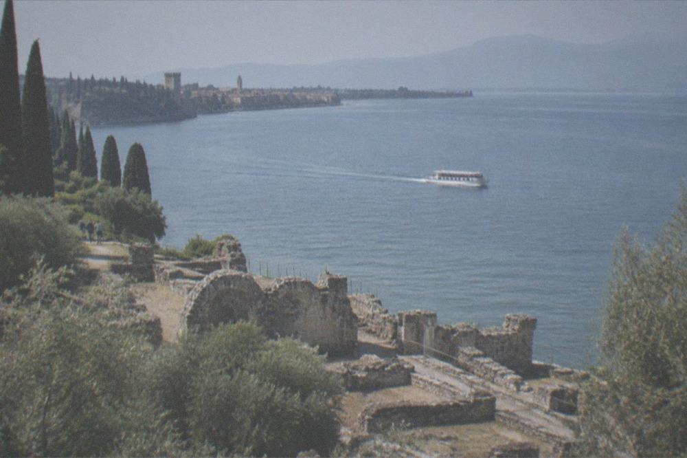 A small cruise boat underway on Lake Garda with Sirmione's peninsula and castle in the distance