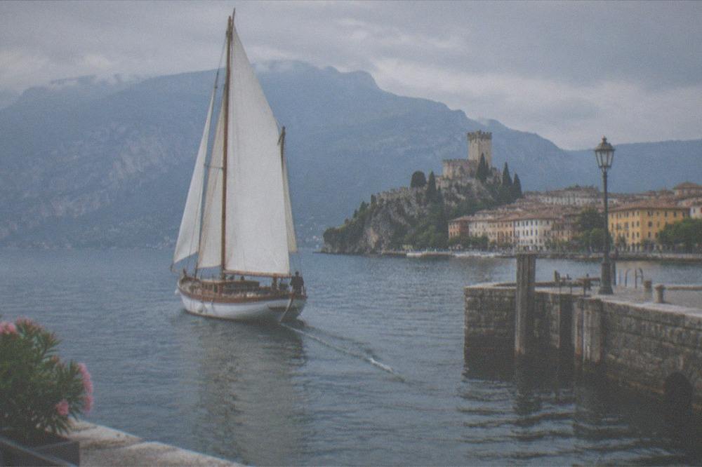 Historic sailboat leaving Malcesine harbour with the mountain ridge behind