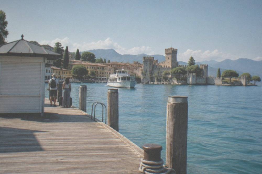 A boat ticket counter and wooden pier on a sunny lakefront with passengers waiting to board