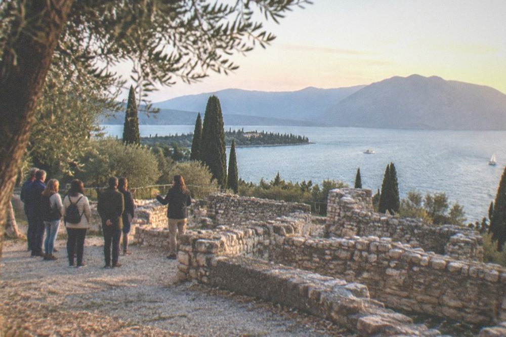A guide speaking to a small group beside ancient Roman stone walls above the lake