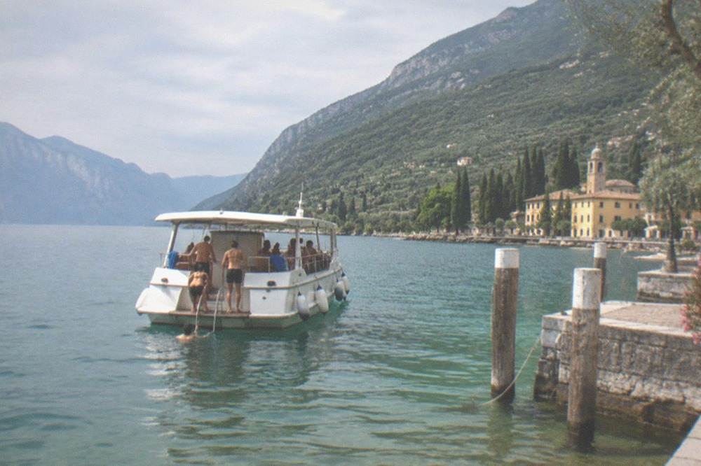 A tour boat with passengers preparing to swim in a quiet Lake Garda bay